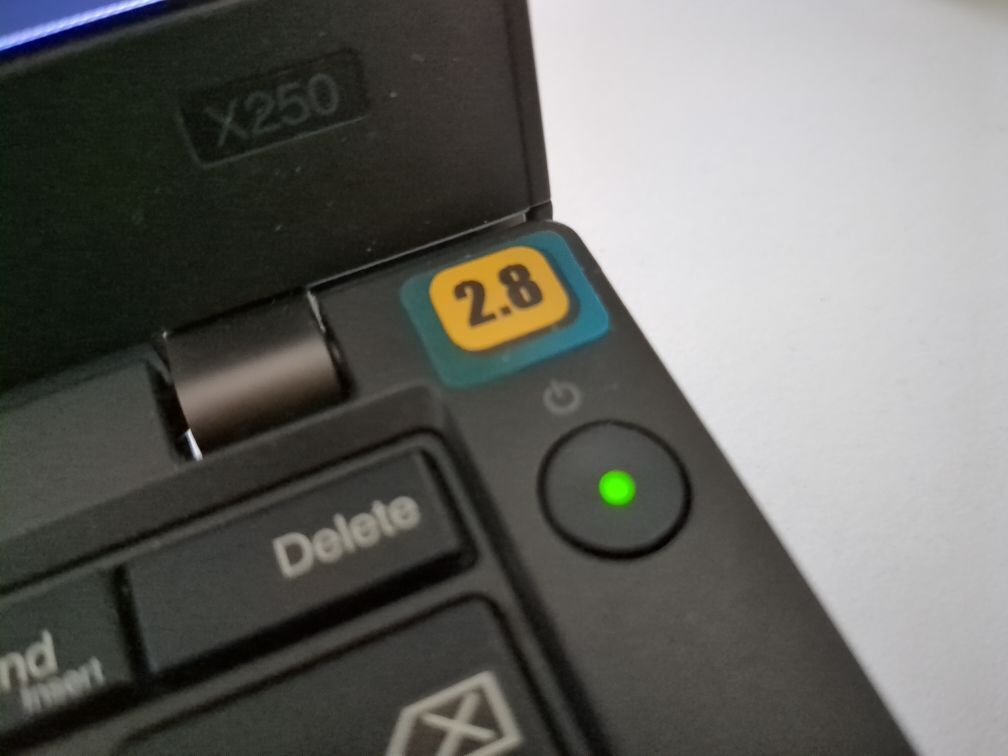 closeup of X250 with an OpenBSD 2.8 sticker covering up a crack in the bezel